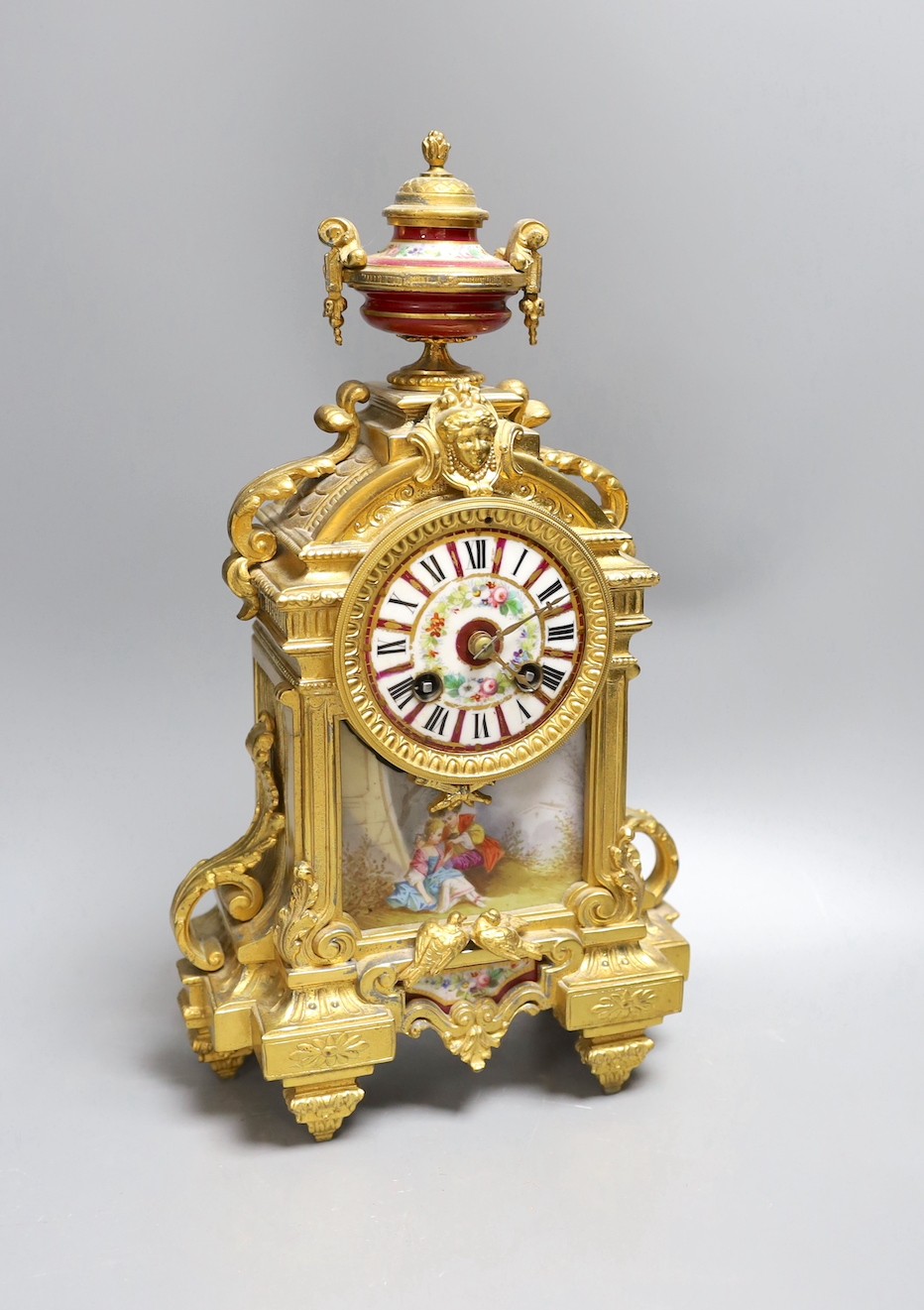 A French gilt spelter mantel clock, with porcelain figurative cartouche and enamelled dial, 37 cms high.